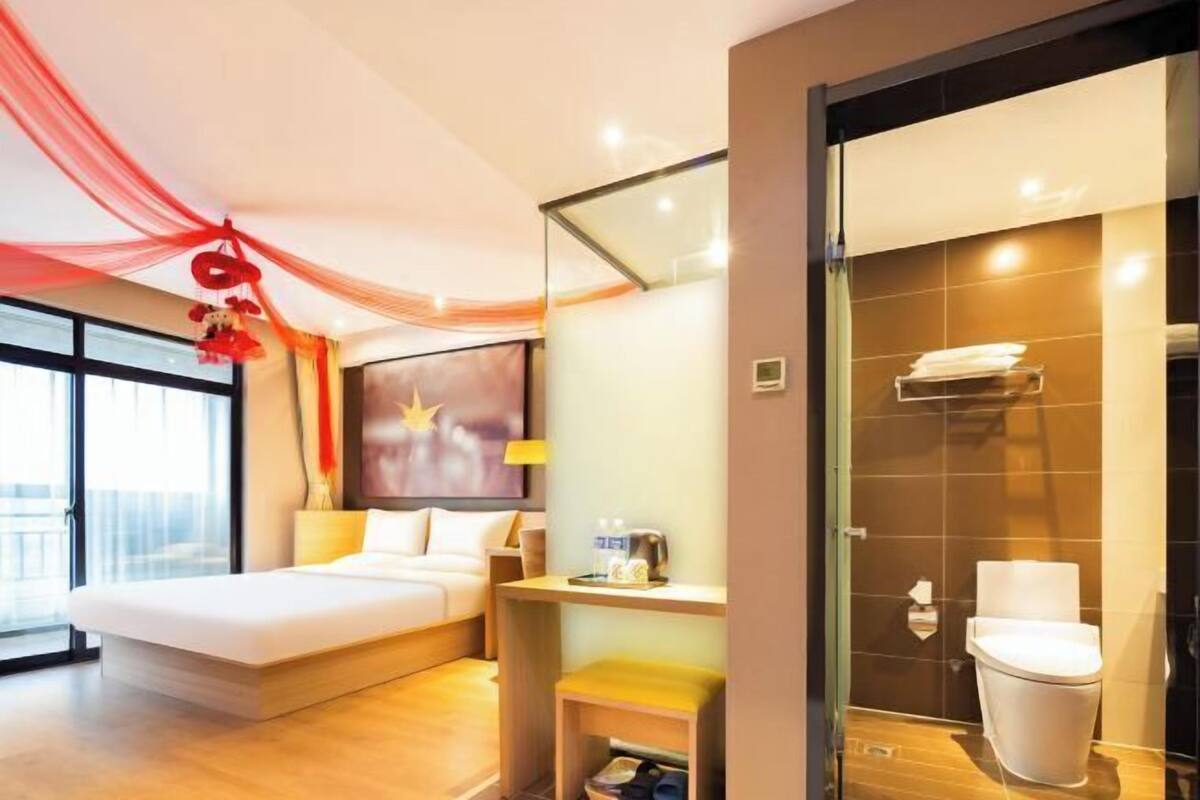 A hotel room with a bed, bedside table, and a glass shower enclosure.