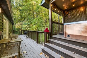 Una terraza de madera con un jacuzzi, asientos exteriores y vistas a un bosque.