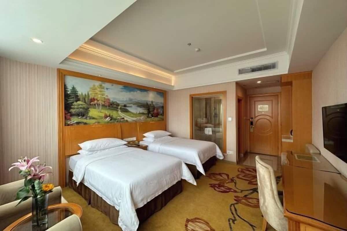 A hotel room with two beds, a painting on the wall, a desk with a chair, and a television.