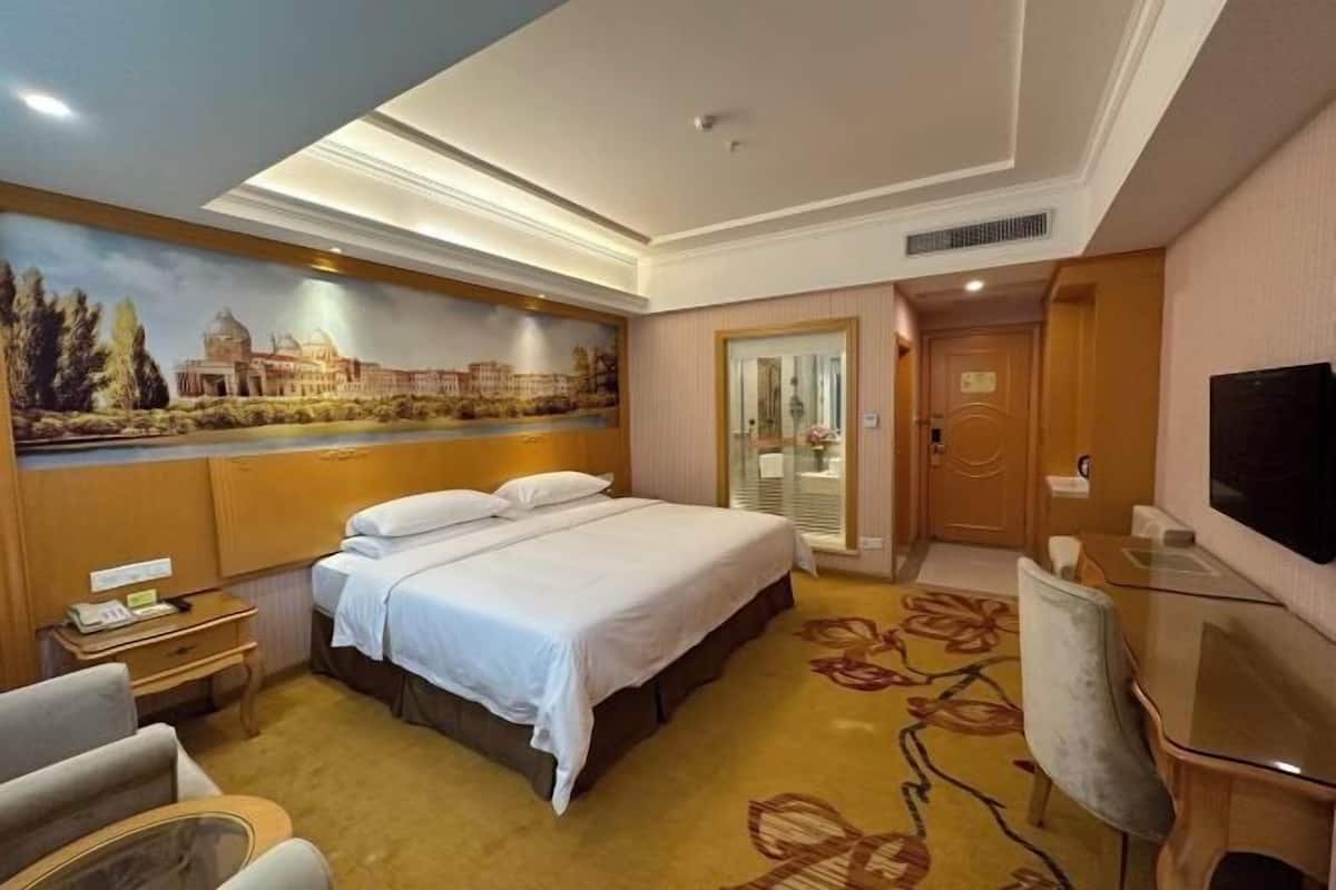 A hotel room with a large bed, a desk with a chair, a television, and a mural on the wall.