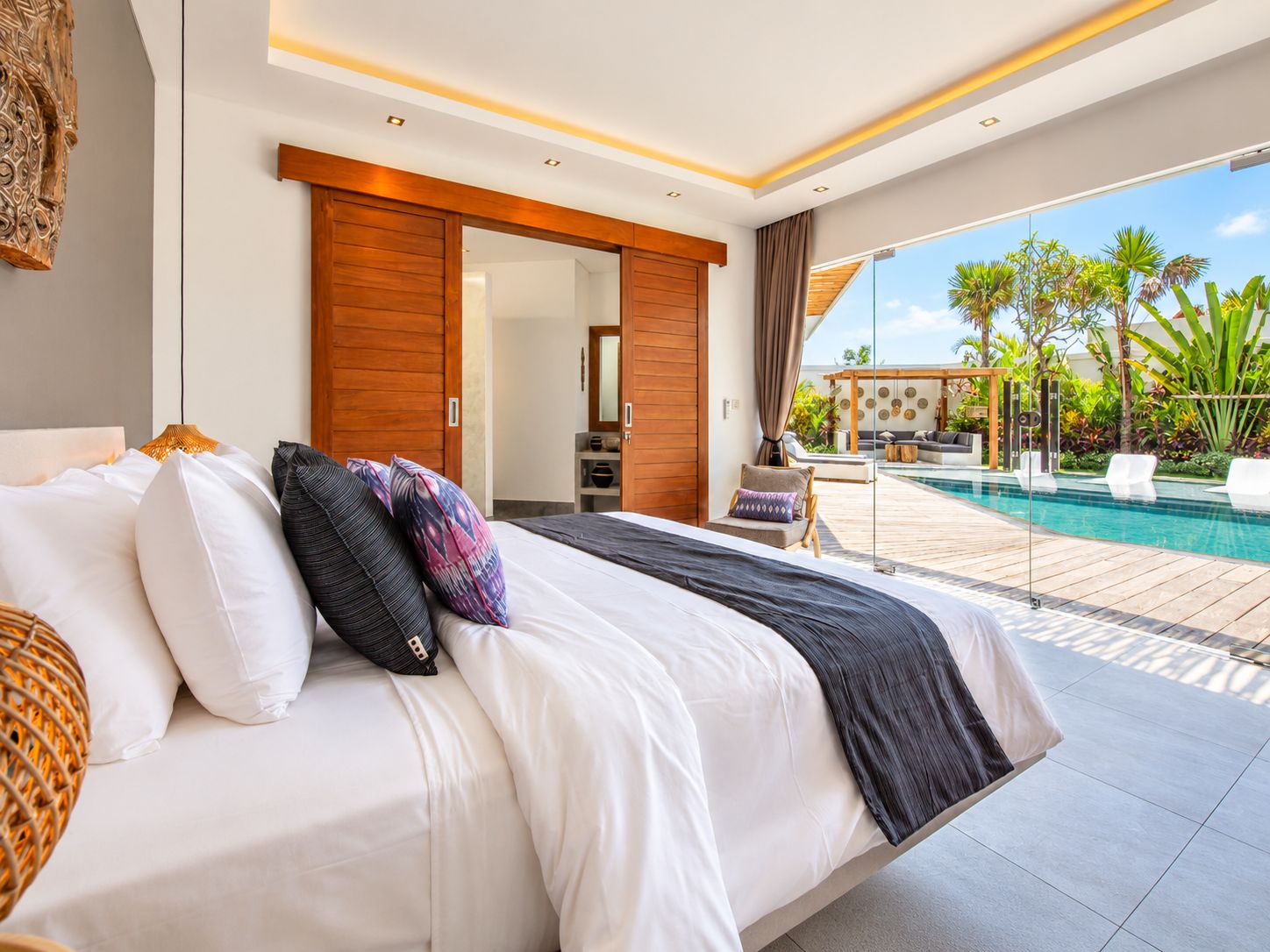 A modern bedroom with a large bed, a wooden wardrobe, and a view of an outdoor swimming pool.