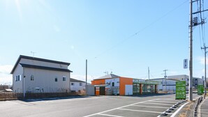 A parking lot with marked spaces, a building with a sign, and a clear sky. - Tabist Capsule Inn Kasakake (Midori)