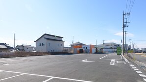 A parking lot with marked lanes and a building with a garage entrance. - Tabist Capsule Inn Kasakake (Midori)