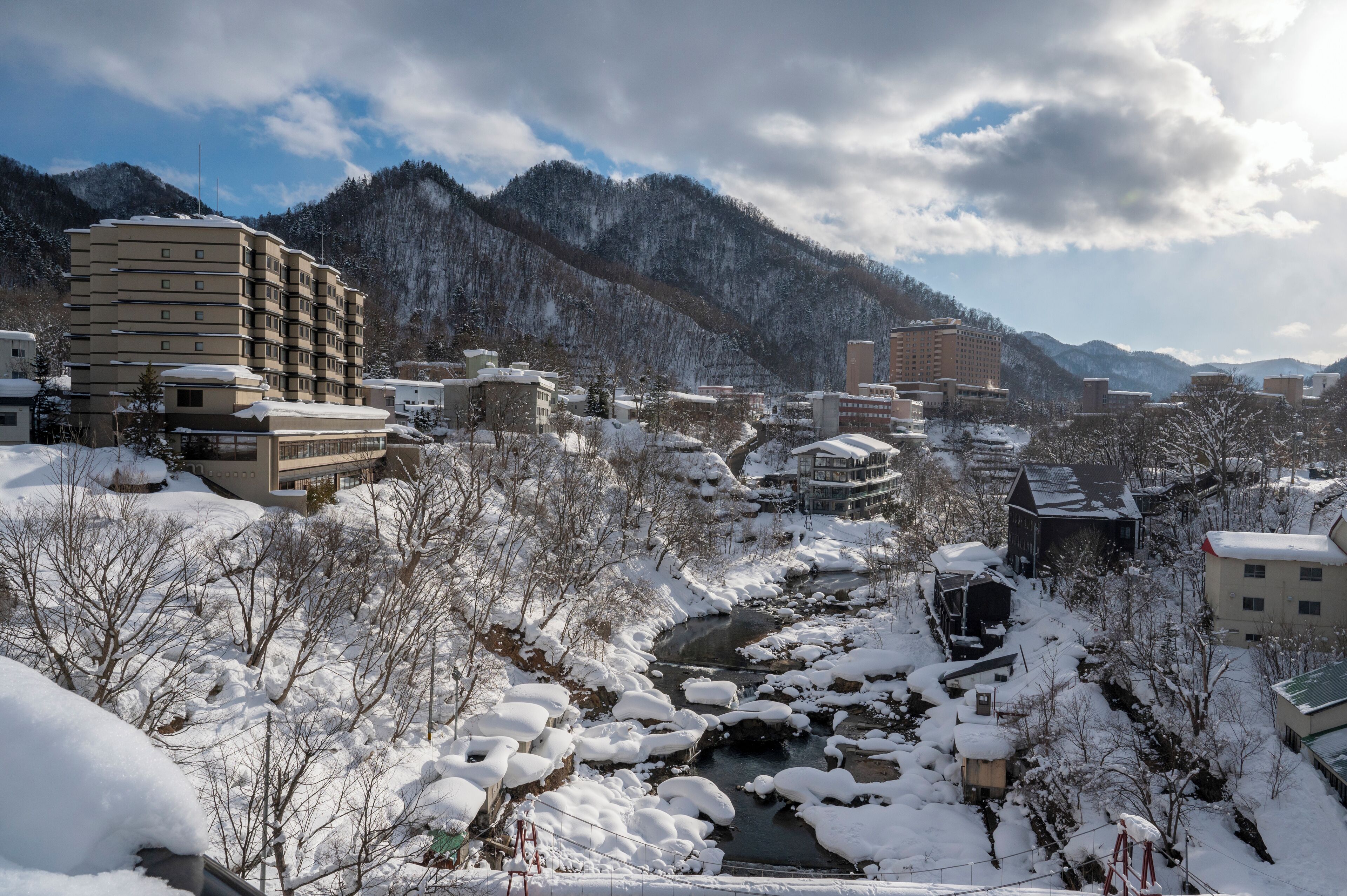 A snow-covered town with a river, buildings, and mountains in the background.