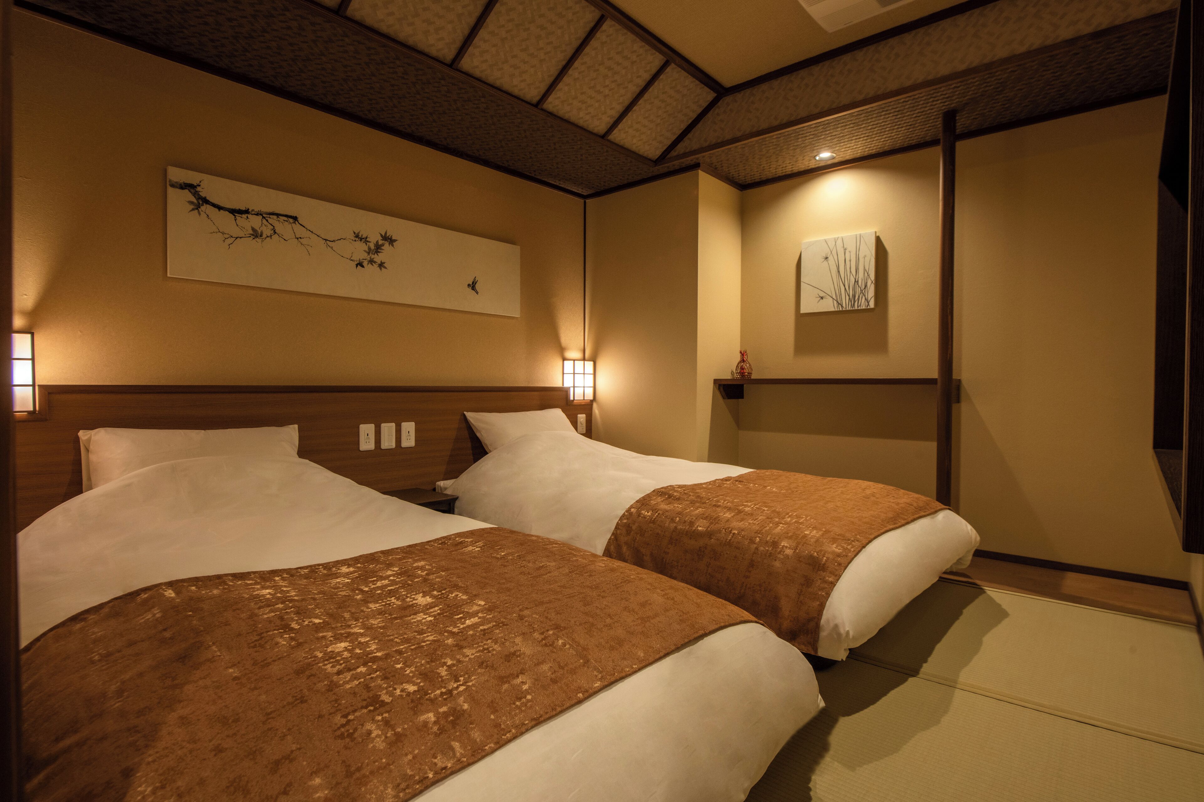 A hotel room with two beds, wooden headboards, wall-mounted artwork, and a traditional Japanese tatami mat floor.