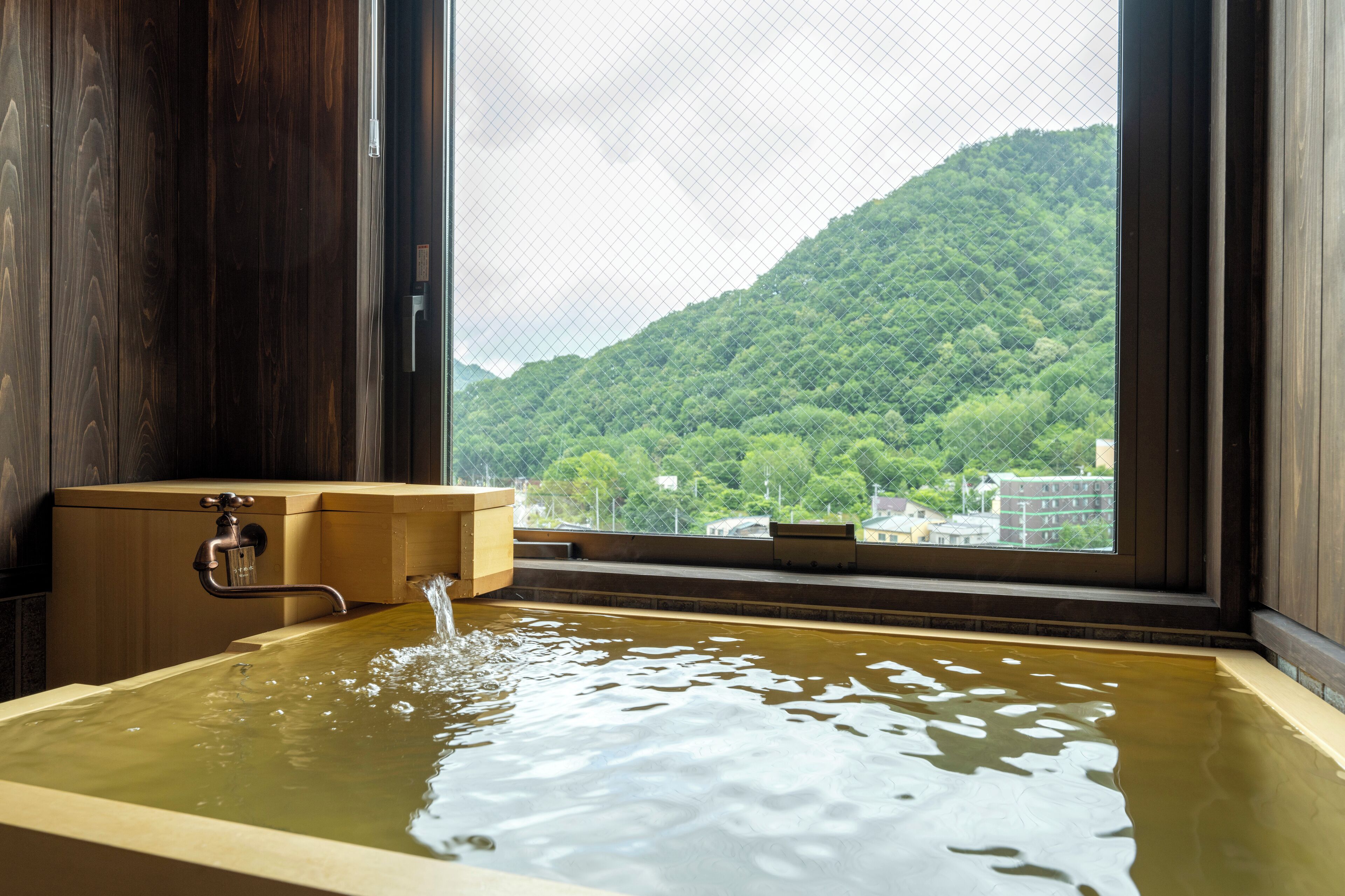 A wooden bathtub with a view of a green mountain through a window.