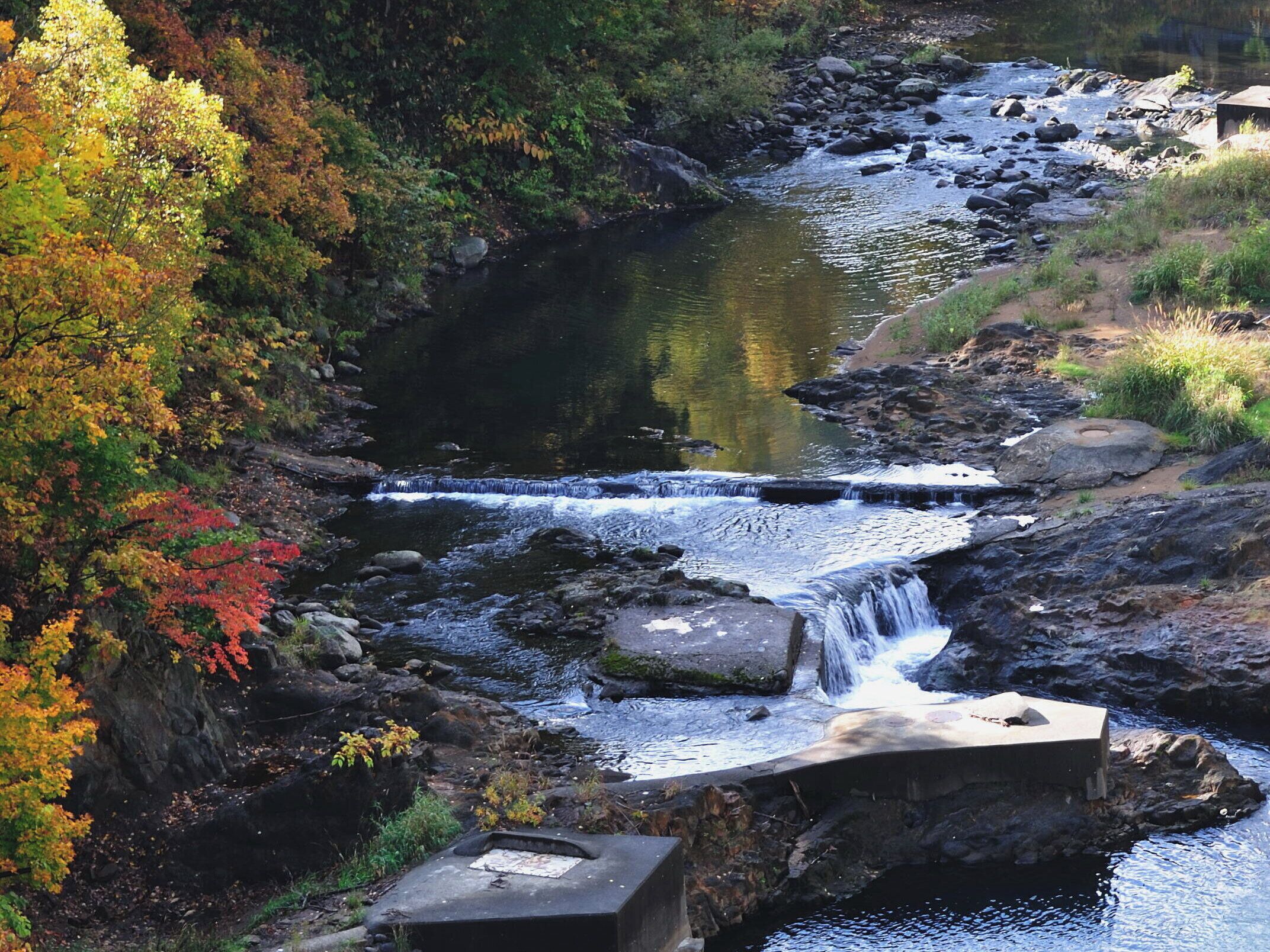 A natural landscape with a waterfall, rocky terrain, and autumn foliage.
