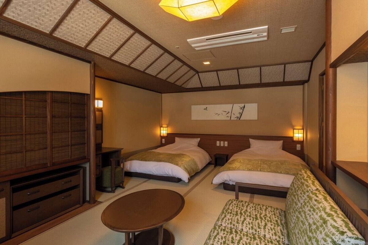 Ein Hotelzimmer mit zwei Betten, einem Fernseher, einem kleinen Tisch und einer traditionellen japanischen Decke.
