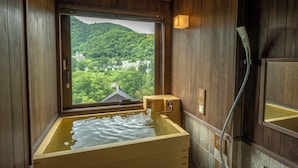 A traditional Japanese onsen with a wooden interior, a large window offering a view of a lush green mountain, and a modern showerhead. - Jozankei Yurakusoan (Sapporo)