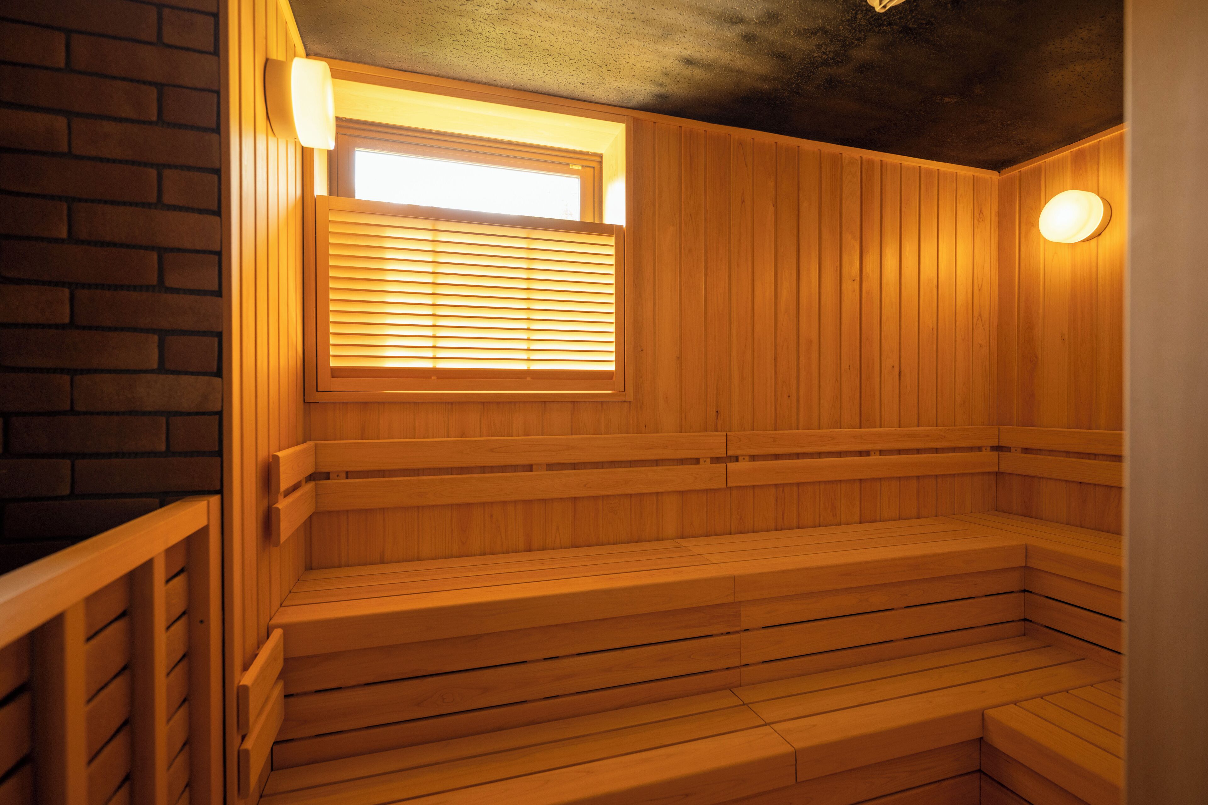 A sauna with wooden benches and a window with blinds.