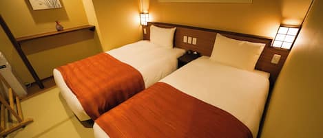 A hotel room with two beds, each with a wooden headboard and white bedding. There are wall-mounted light fixtures and a small shelf with a decorative item.