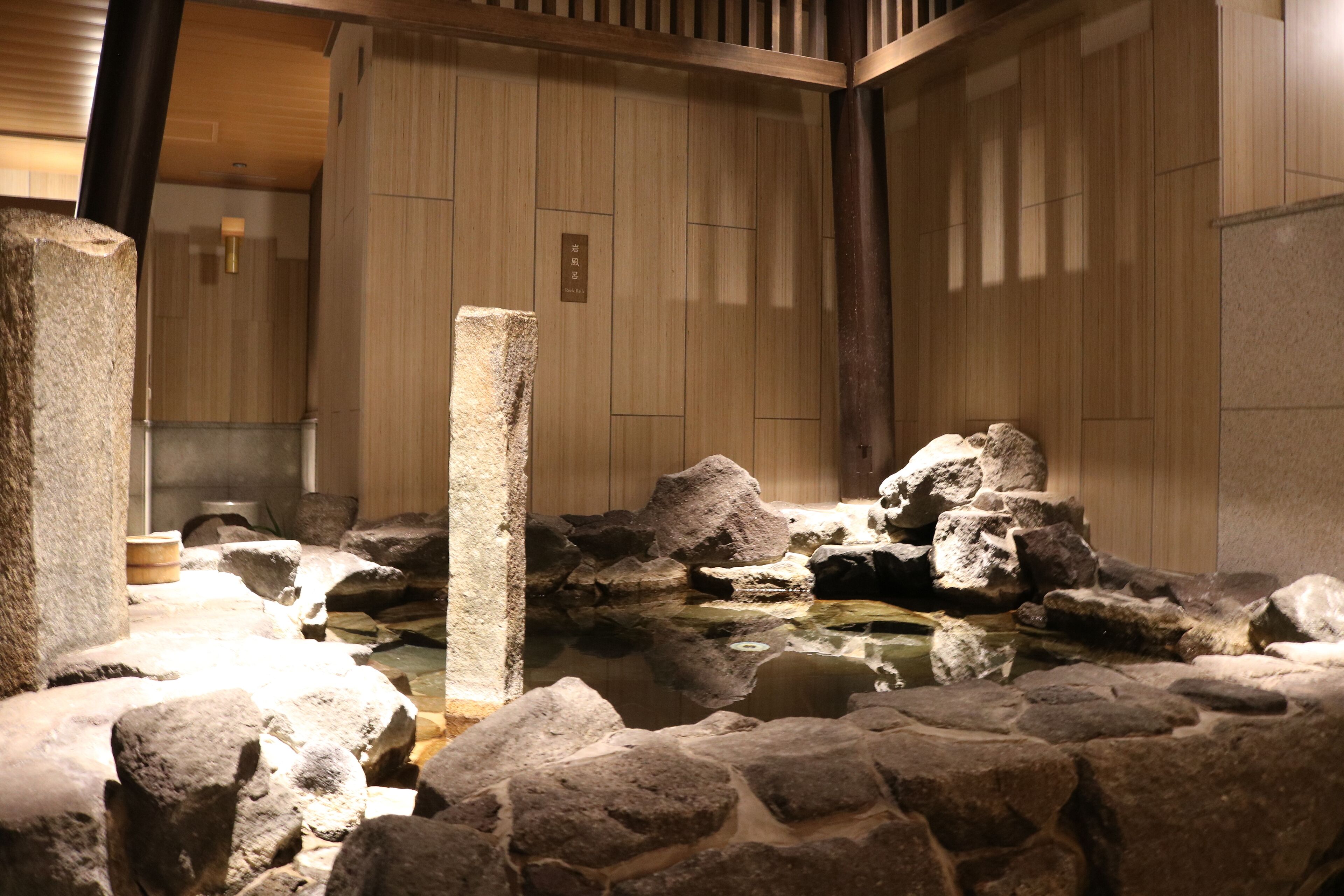 A traditional Japanese onsen with stone baths, wooden walls, and a tiled floor.
