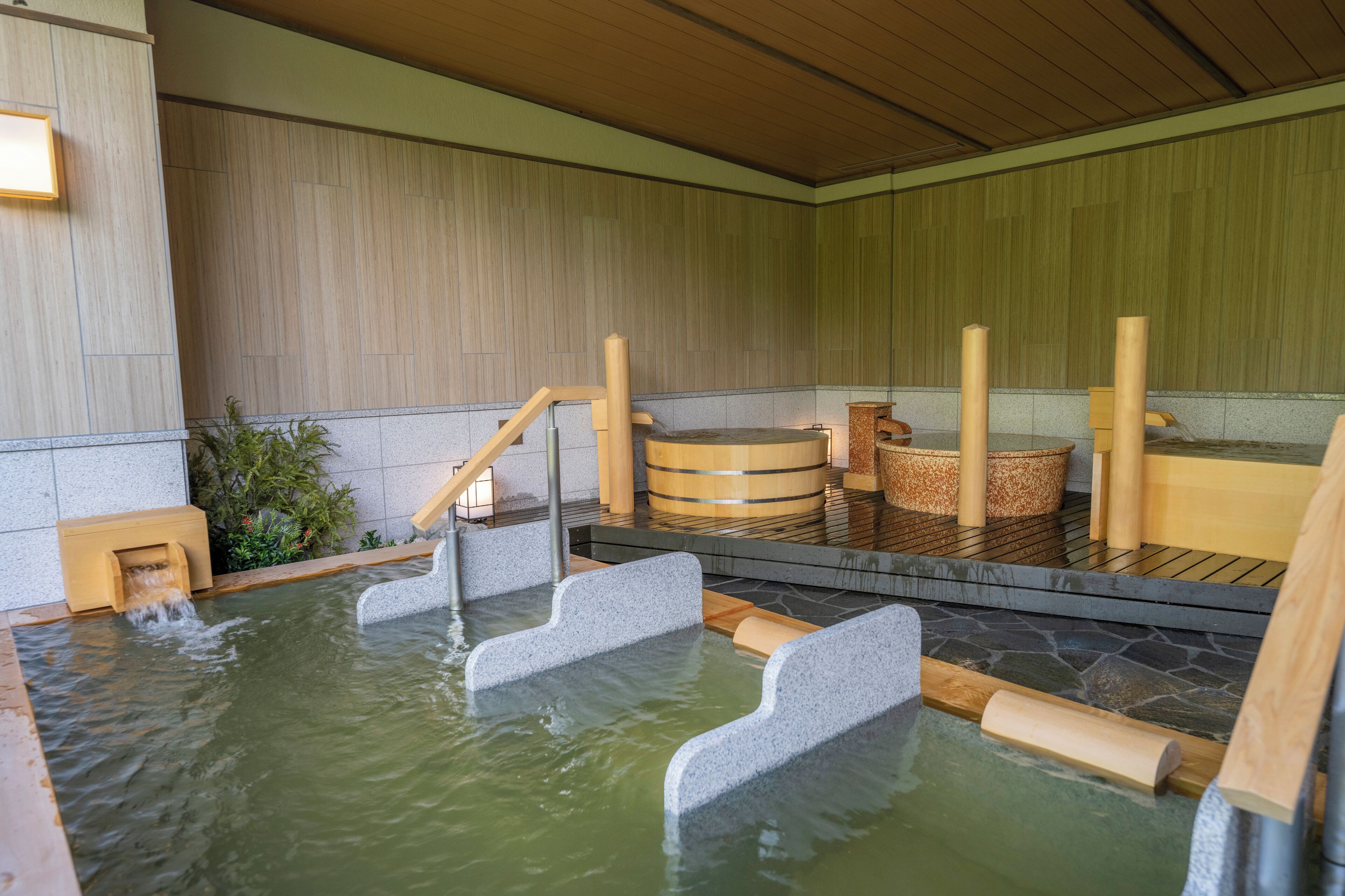 Een traditioneel Japans onsen met stenen trappen die leiden naar een warmwaterbron, houten banken en een houten plafond.