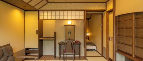 A traditional Japanese-style room with tatami flooring, a low wooden desk, a cushioned seating area, and a sliding door leading to a bedroom.