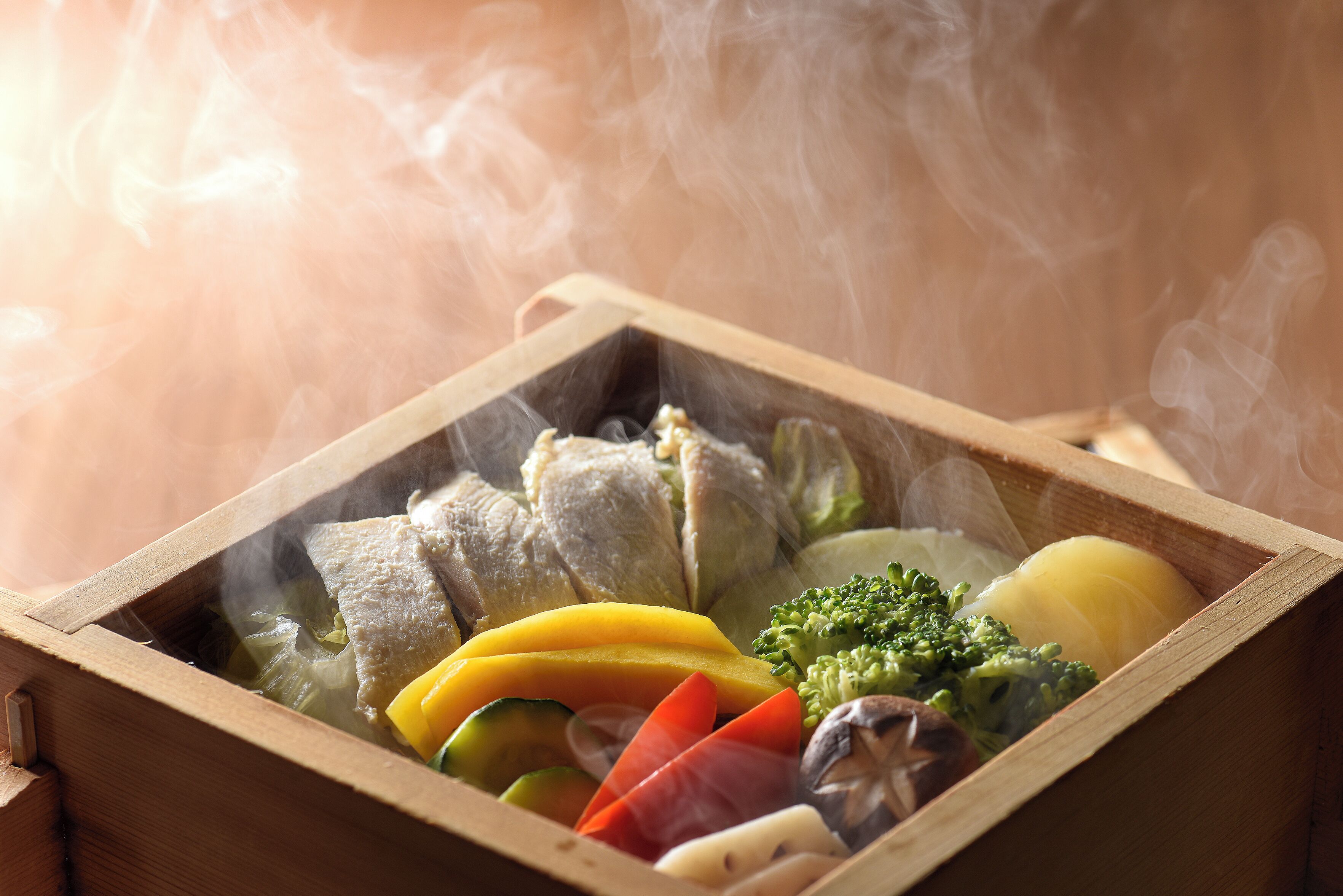 A wooden box containing various vegetables and a piece of meat, with steam rising from the contents.