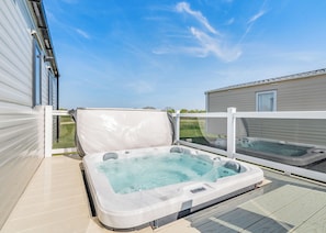 A hot tub on a deck with a view of a house and clear sky.