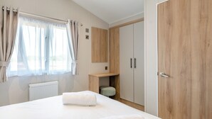 A bedroom with a bed, a wooden wardrobe, a small wooden table, and a radiator. - Platinum Caravan 6 Berth (3 bed) (Pet) (Skegness)