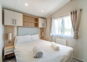A bedroom with a bed, bedside tables, a wardrobe, a window with curtains, and a radiator.