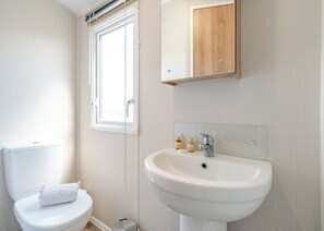 A bathroom with a toilet, a sink, and a window. - Platinum Caravan 6 Berth (3 bed) (Pet) (Skegness)