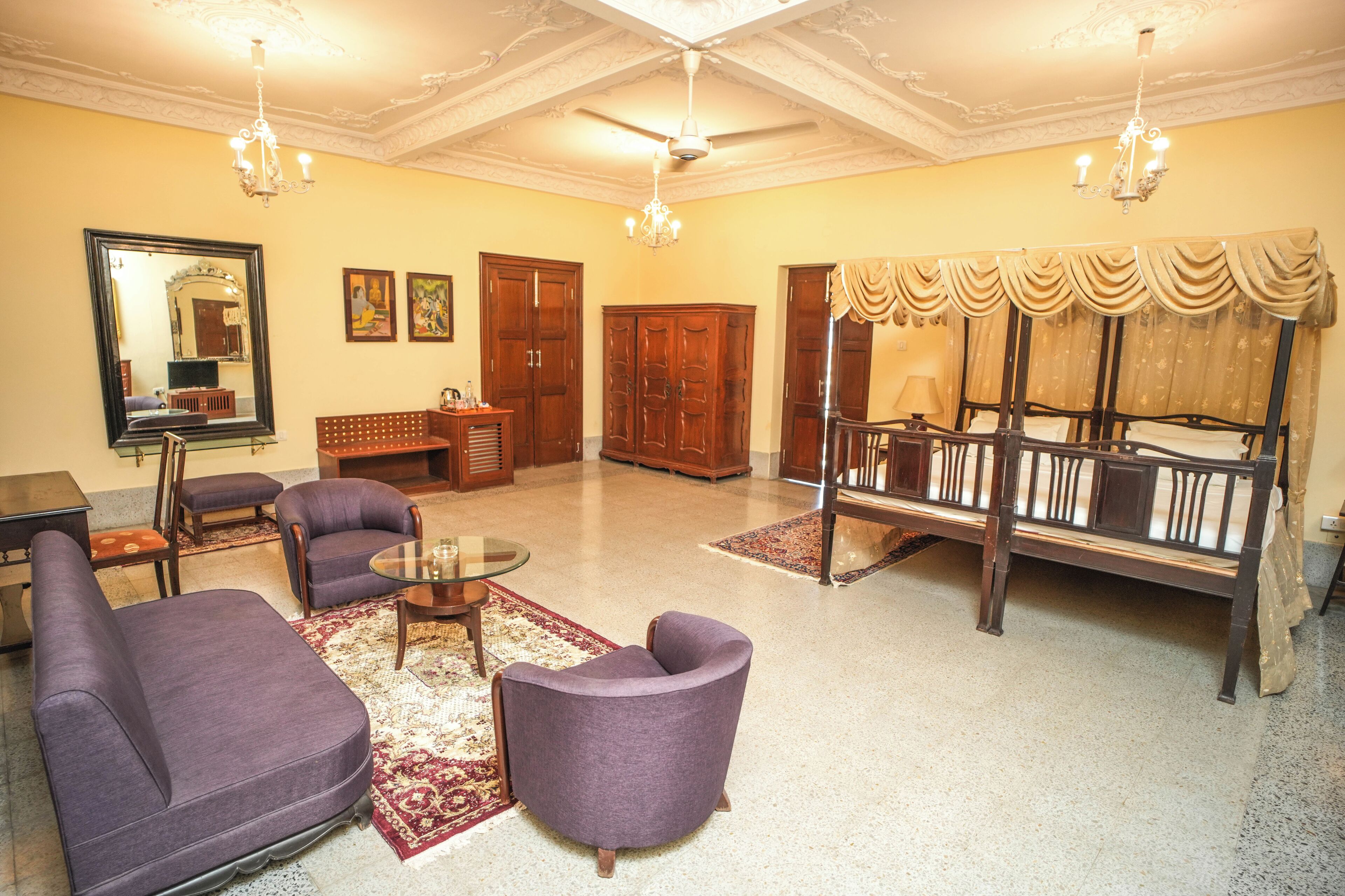 A spacious living room with a large sofa, armchairs, a glass coffee table, and a wooden bed with a canopy.