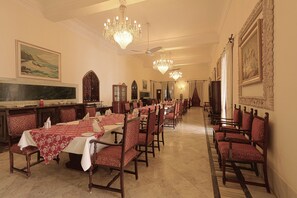 A formal dining room with multiple tables, chairs, chandeliers, and framed artwork on the walls. - Nilambag palace (Bhavnagar)