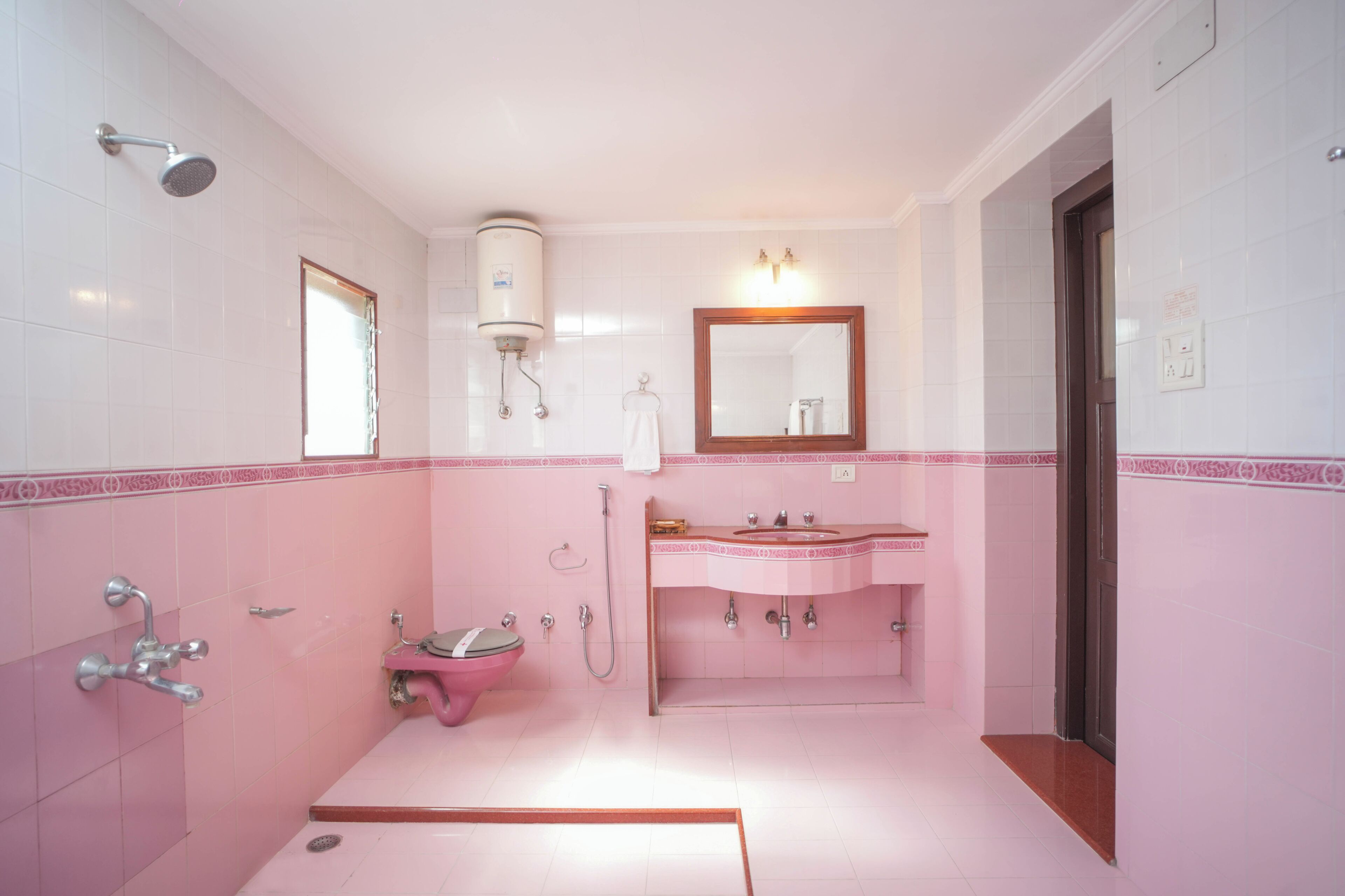 Casa de banho com esquema de cores rosa e branco, um lavatório, uma sanita, um chuveiro e um espelho.