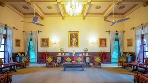 A spacious room with a central bench, two ceiling fans, and a chandelier. - Nilambag palace (Bhavnagar)