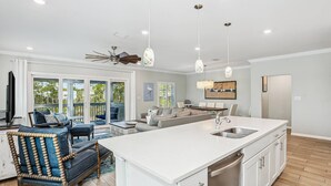 Un vaste espace de vie comprenant une grande cuisine avec un îlot central, un ventilateur de plafond et une vue sur l’extérieur.
