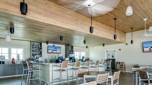 Un grand espace bar avec de nombreux coins salon, un téléviseur fixé au mur et un plafond en bois.