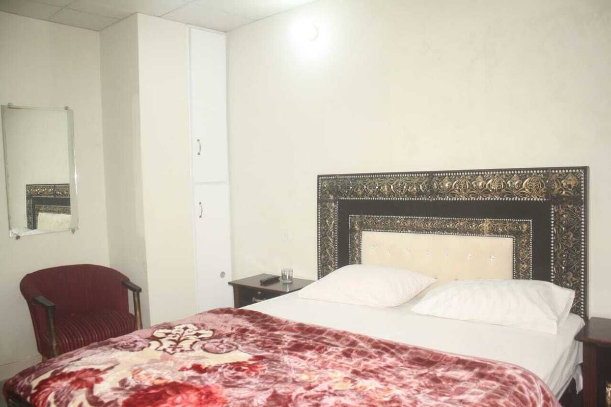 Una habitación con cama, una silla, una mesita de noche, un espejo y un armario.
