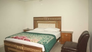 A bedroom with a bed, a wooden nightstand, a chair, and a ceiling fan. - Hotel Shadman (Lahore)