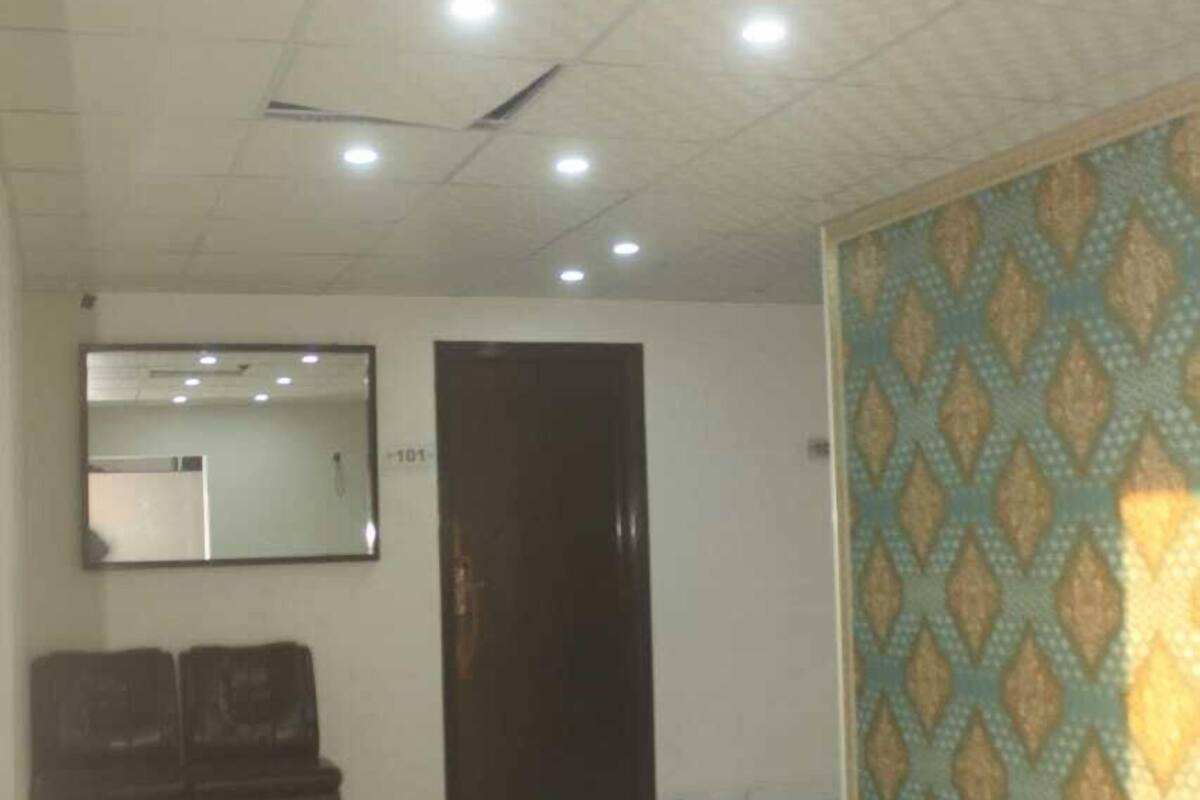 Una habitación amplia con suelo de baldosas, una puerta oscura, un espejo en la pared y un papel pintado decorativo en una pared.