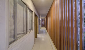 A hallway with a wooden panel wall, a tiled floor, and large windows on one side. - Itsy Hotels Sky Vista (Pune)