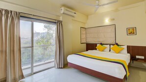 Habitación de hotel con una cama grande, ventilador de techo, aire acondicionado y vistas al exterior por una ventana.