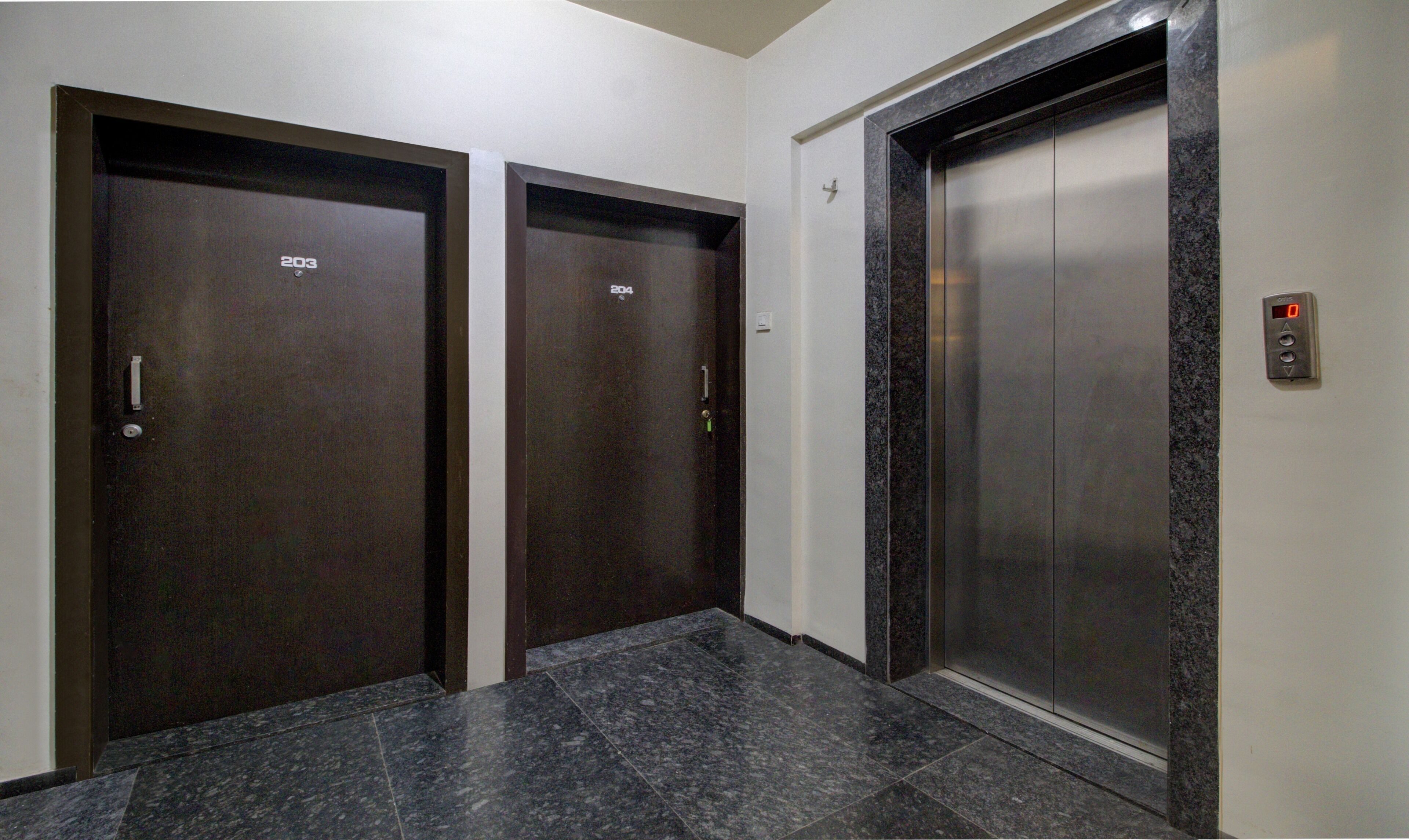 Two elevator doors with numbers 203 and 204, a marble-tiled floor, and a control panel with a digital display.