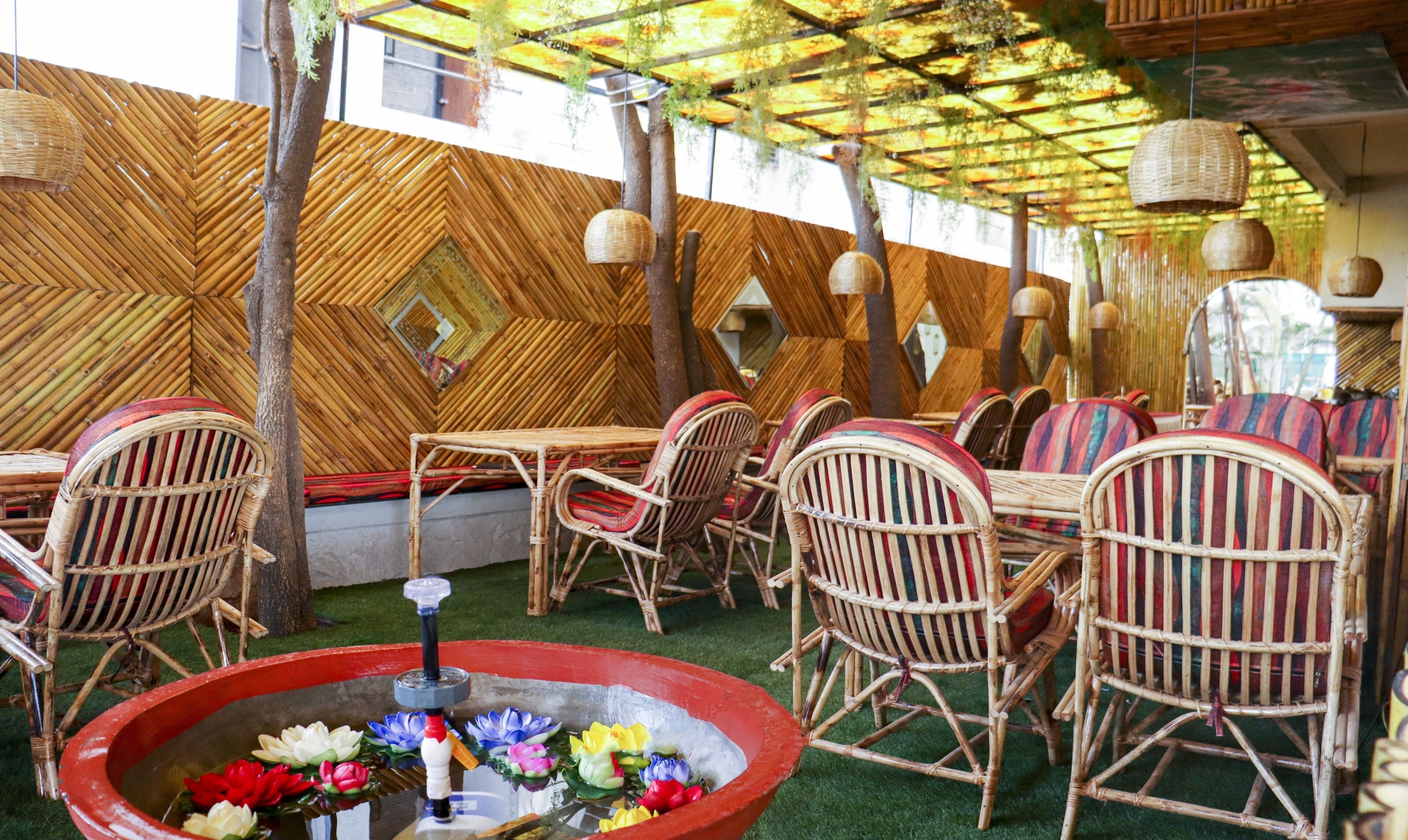An outdoor seating area with bamboo walls, wicker furniture, and hanging lights.