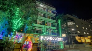 Un edificio de varios pisos con un restaurante llamado "Bamboo Pot" en la planta baja, que cuenta con un letrero de neón y un área de estar al aire libre.