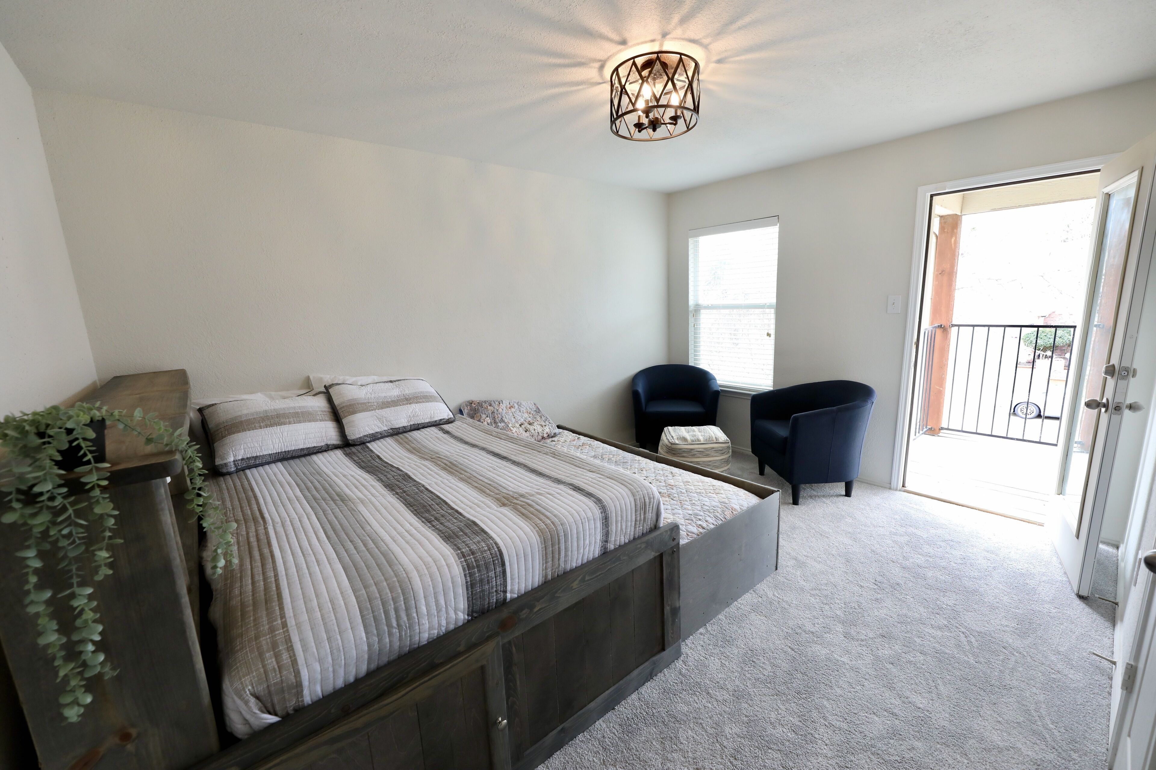 A bedroom with a bed, a chair, a small table, and a door leading to a balcony.