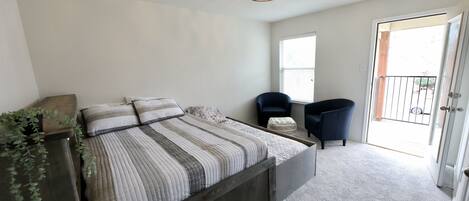 A bedroom with a bed, a chair, a small table, and a door leading to a balcony.