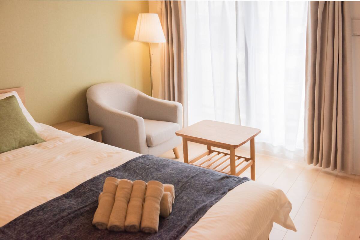 A hotel room with a bed, a chair, a small table, and a lamp.
