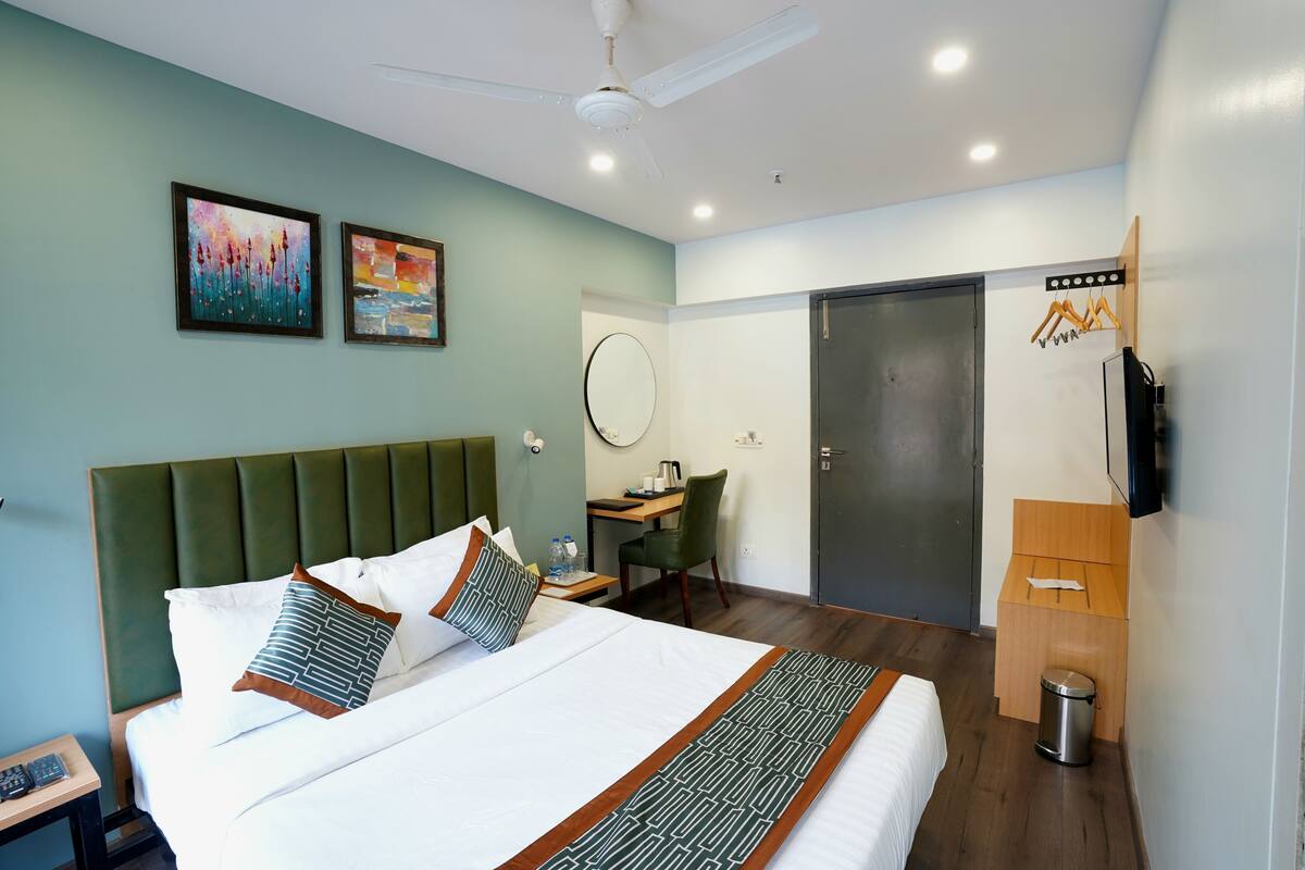 A hotel room with a bed, a desk, a chair, a TV, and a wardrobe.