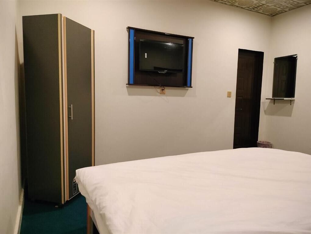 A hotel room with a bed, a wardrobe, a television mounted on the wall, and a door.