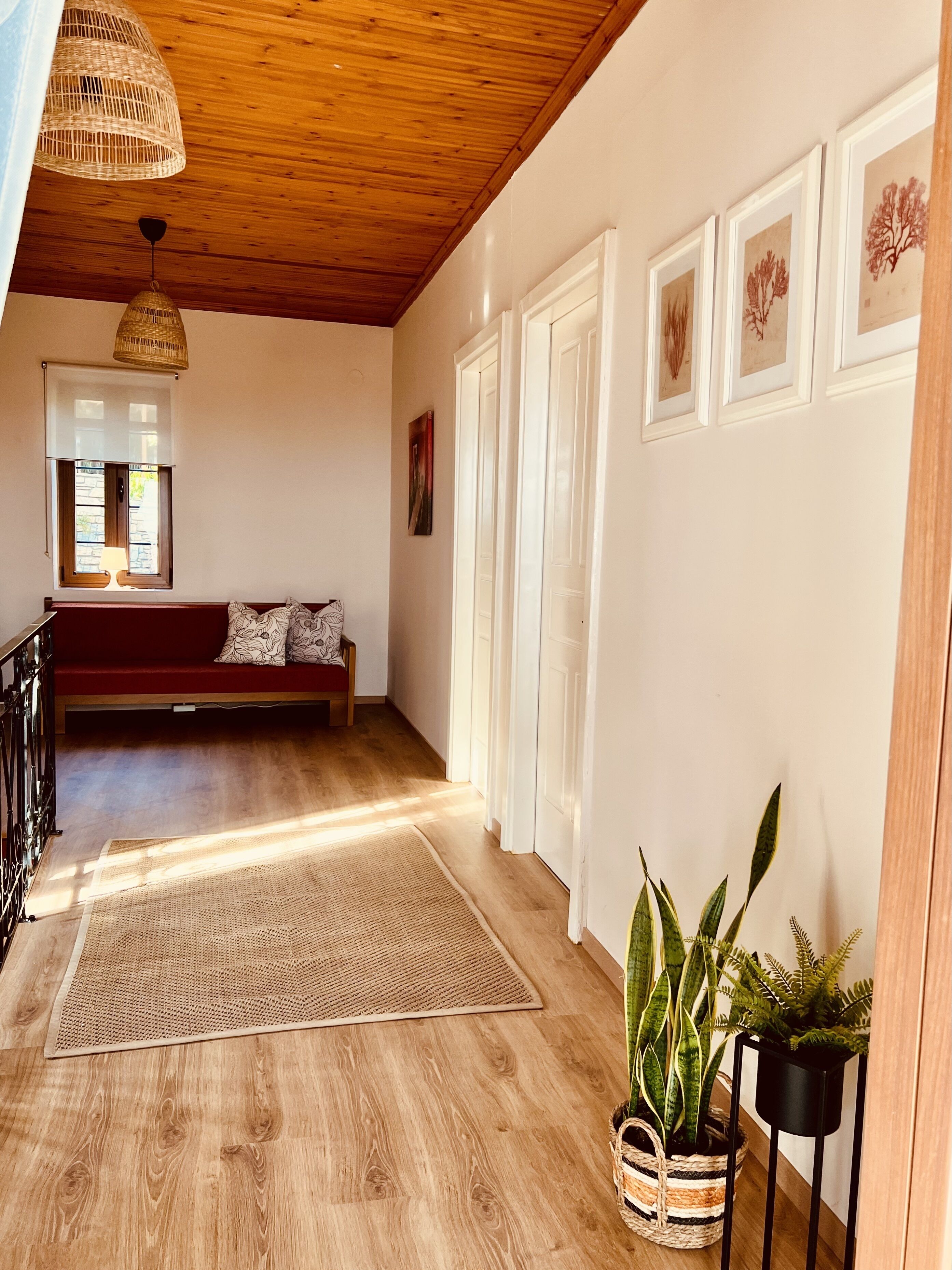 Un couloir au plancher de bois, agrémenté d’un tapis tissé, d’un banc rouge et d’œuvres d’art encadrées accrochées au mur.