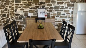 Un'area pranzo con un tavolo di legno e sedie nere, una parete in pietra, un frigorifero bianco e un quadro appeso al muro.