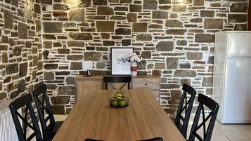 Un coin repas avec une table en bois et des chaises noires, un mur en pierre, un réfrigérateur blanc et un tableau encadré accroché au mur.