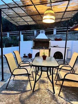 An outdoor patio with a table and chairs, a grill, and a pergola with a hanging light fixture.