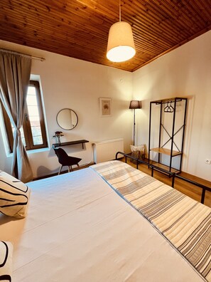 A bedroom with a bed, a desk, a chair, a radiator, a mirror, a lamp, and a wardrobe.