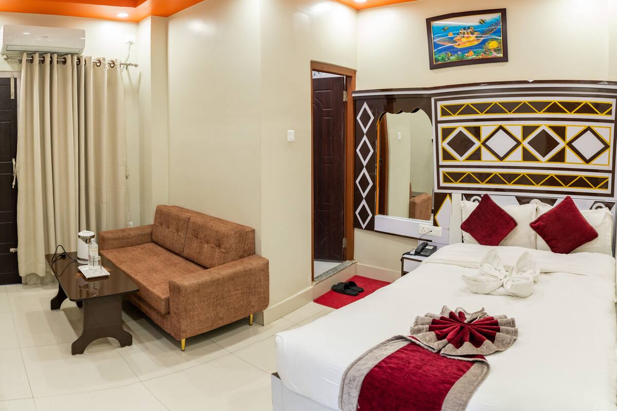 A hotel room with a bed, a sofa, a small table, a mirror, and a door.