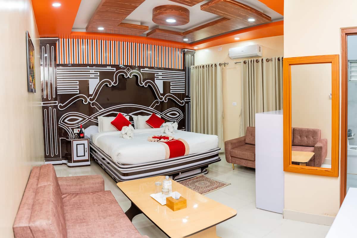 A modern hotel room with a large bed, a sofa, a small table, and a bathroom visible through an open door.