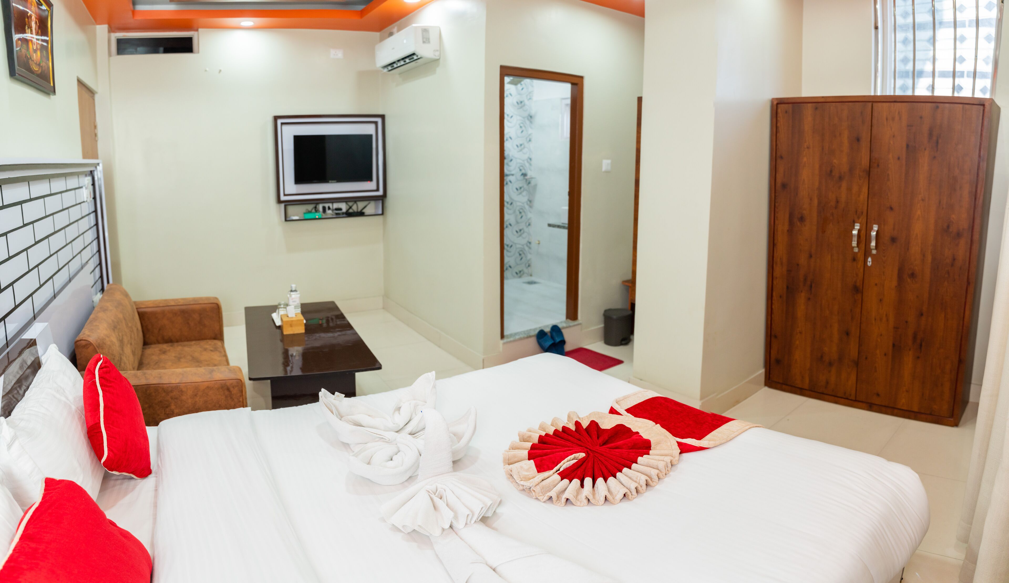 A hotel room with a bed, a TV, a wardrobe, a sofa, and a small table.